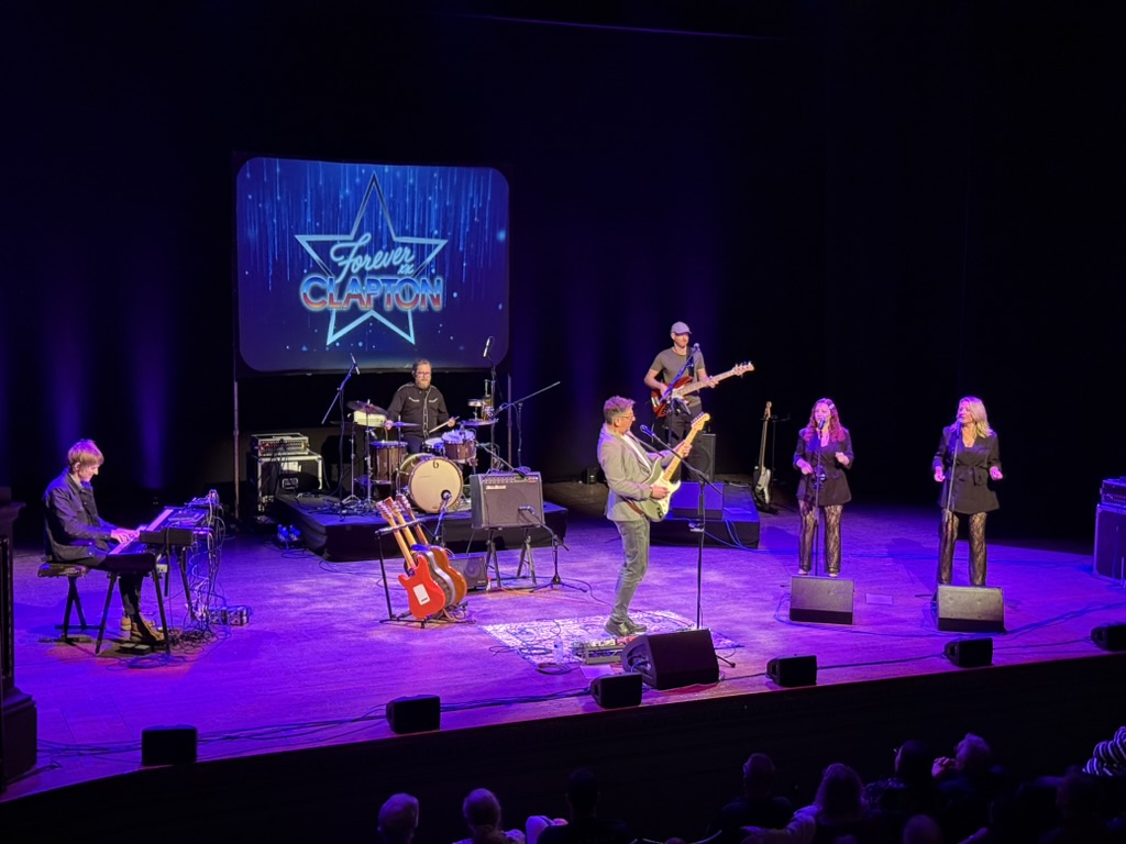 Forever Clapton band performing together on a purple-lit theatre stage